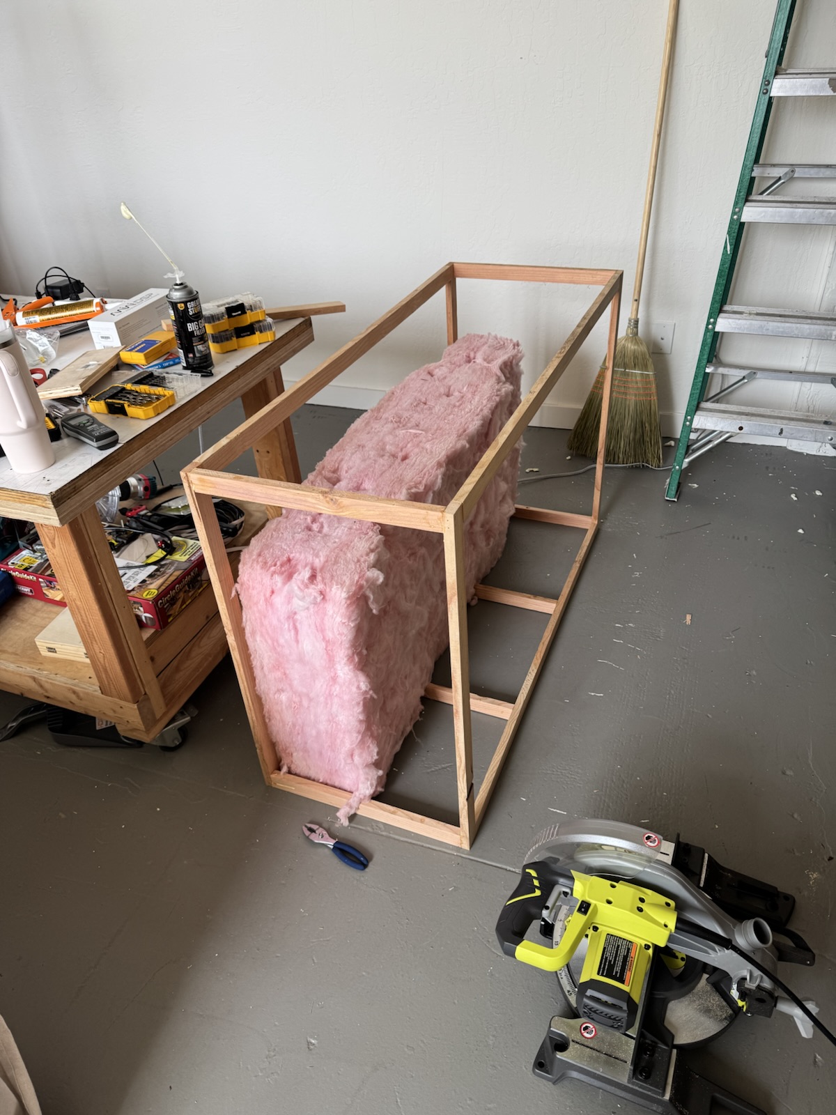 A timber frame on the workshop floor being filled with pink fibreglass batts.