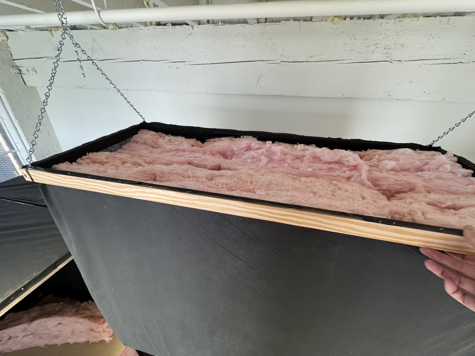 Close-up of a hung absorber from above: a black fabric box packed with pink fibreglass, held on chains.