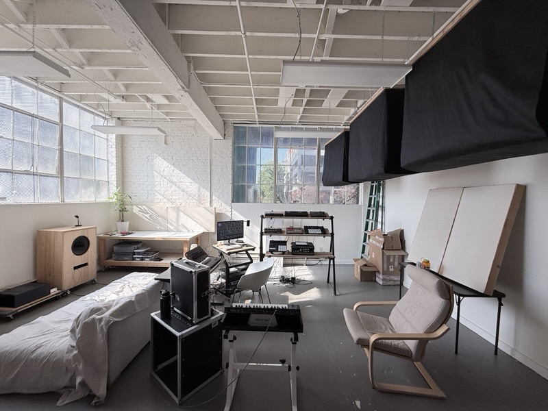 The room looking away from the window: hanging black absorbers under the roof trusses, a couch and an armchair.